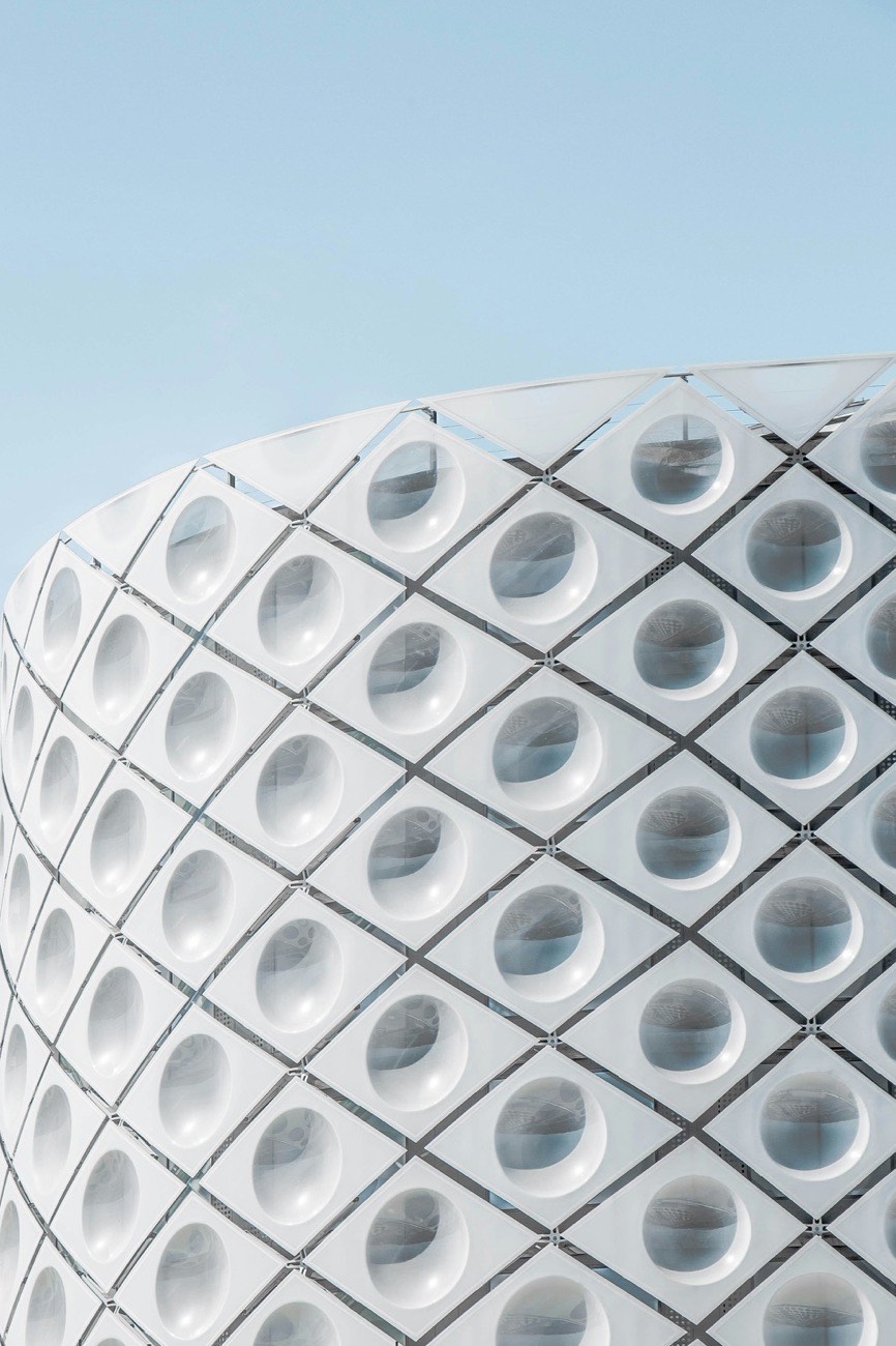 Detail of a curved white building facade with a repeating grid of circular openings
